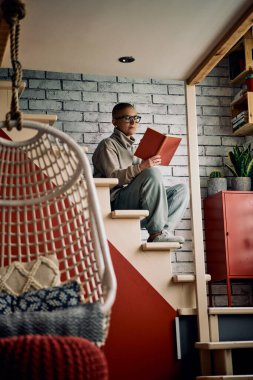 Evde merdivenlerde oturan kısa saçlı yaşlı kadın ilginç bir kitap okuyor..