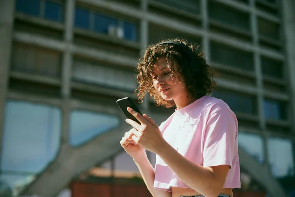 Милая Молодая Женщина Сидит Улице Наушниках Выбирает Хорошую Музыку Телефоне — стоковое фото
