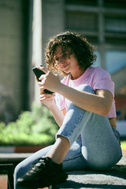 Dışarıda oturan, kulaklık takan ve müzik dinleyen sevimli genç bir kadın..