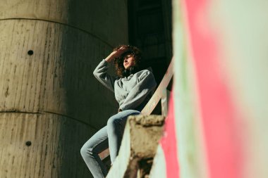 Kıvırcık saçlı genç kız dışarıda oturuyor ve etrafa bakıyor..