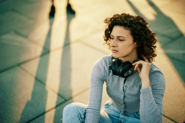Νεαρή Γυναίκα Κάθεται Στο Δρόμο Εξωτερικούς Χώρους Ακουστικά Γύρω Από — Φωτογραφία Αρχείου