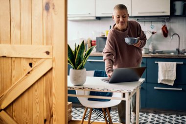 Yetişkin bir kadın mutfakta duruyor ve kahvaltısını yapıyor..