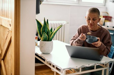 Yetişkin bir kadın mutfakta duruyor ve kahvaltısını yapıyor..
