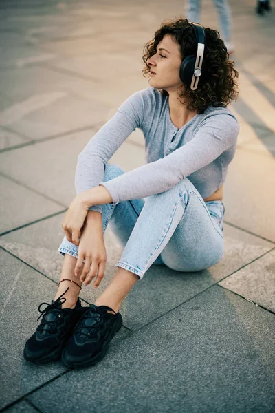 Una Giovane Donna Con Capelli Ricci Seduta Una Strada Ascolta — Foto Stock