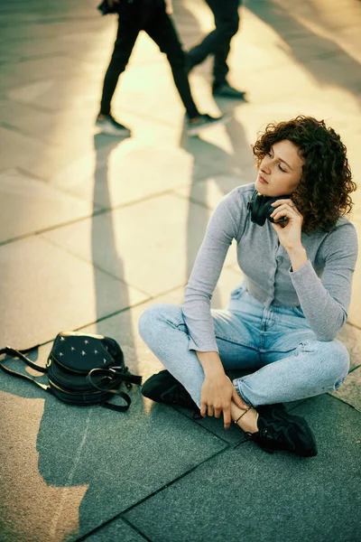 Una Joven Está Sentada Calle Con Auriculares Alrededor Del Cuello — Foto de Stock