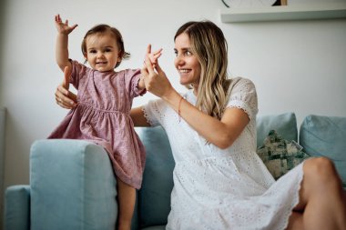 Genç ve güzel anne sevgili kızıyla oynuyor. Bebek çok mutlu ve kollarını havada tutuyor..