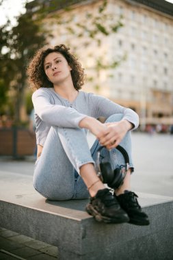 Dışarıda oturan genç bir kadın, kulaklıkları elinde ve ürpertici..