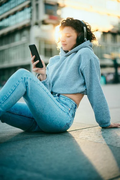 Una Mujer Joven Está Sentada Calle Con Auriculares Usando Teléfono — Foto de Stock