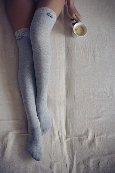 Γυναίκα που κάθεται στο κρεβάτι με το φλυτζάνι του καφέ — Φωτογραφία Αρχείου