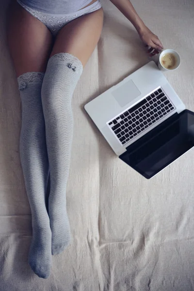 Mulher sentada na cama com xícara de café e laptop — Fotografia de Stock