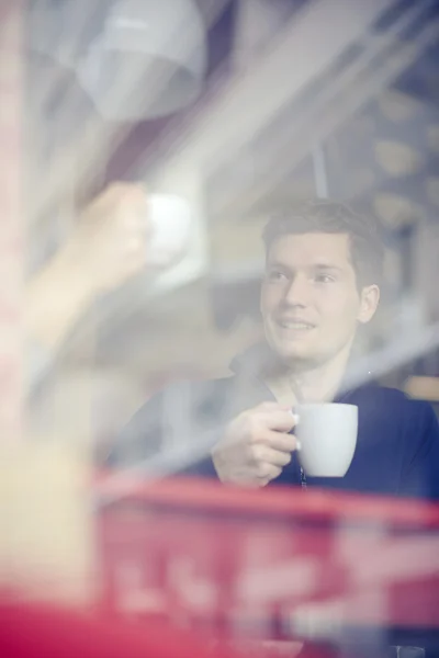 Man with coffee cup looking through window in cafe — Stock Photo, Image