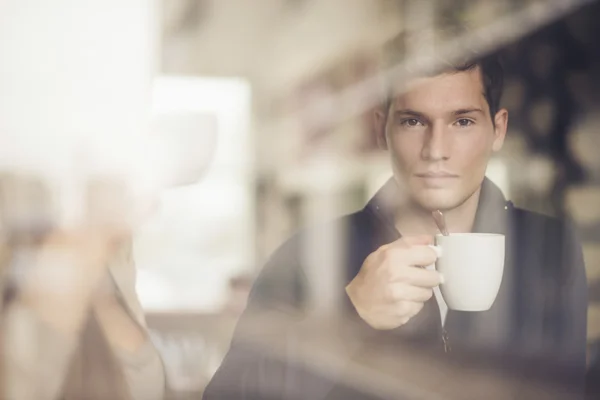 Man met koffiekopje kijken via venster in café — Stockfoto