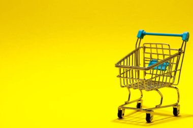 Sarı arka planda süpermarket arabası. Uzayı kopyala Alışveriş konsepti. Zıplayan araba.