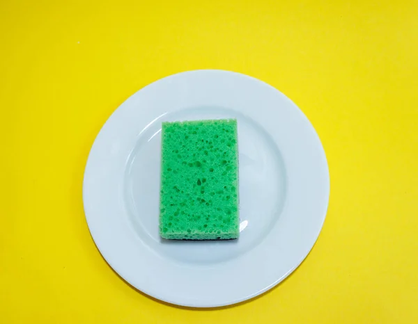 Cleaning sponge on a white plate on a yellow background.Flat lay