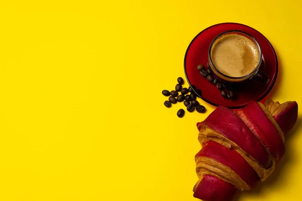 a simple breakfast at home. Cup of hot coffee with red croissant on a yellow background with copy space. Light breakfast concept.