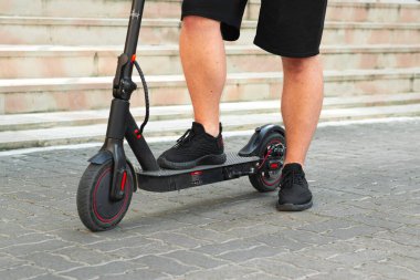 Sokakta gün batımında scooter süren bir çocuk. Adam şehrin arka planında elektrikli scooter kullanıyor. E-scooter teknolojisi kavramı.