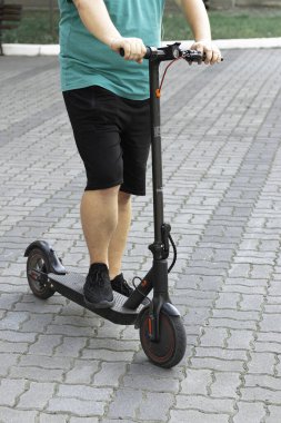 Sokakta gün batımında scooter süren bir çocuk. Adam şehrin arka planında elektrikli scooter kullanıyor..