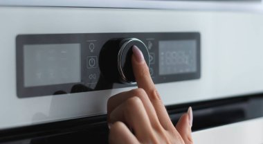 Kadın parmağı modern elektrikli fırın panelinin düğmesine basıyor. Teknoloji konsepti. Kadın parmağına odaklan..
