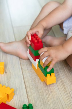 Küçük çocuk yerde plastik renkli oyuncak bloklarıyla oynuyor. Evde renkli plastik tuğlalarla oynayan çocukların ellerini kapayın. Yeni yürümeye başlayan çocuk parlak tuğlalardan eğleniyor ve inşa ediyor..