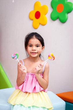 Sevimli çocuğun portresi elinde şeker, neşeli kız çocuğu renkli gökkuşağı lolipopuyla eğleniyor