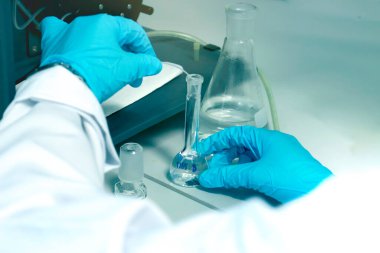 ICP çözeltilerindeki ağır metallerin seviyelerini belirlemek için deney yapmak için hacimli matara eldiveni kullanan mavi kimyasal koruyucu bir bilim adamı eli (İndüktif Eşleştirilmiş Plazma spektrometresi). Kimya laboratuvarında çalışan kimyager.