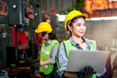 Fabrika imalatında dizüstü bilgisayar kullanan endüstriyel mühendis kadın kask takıyor. Endüstride çalışan genç ve güzel bir kadın.