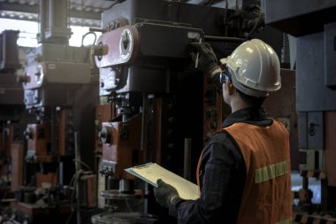 Miğfer ve güvenlik gözlüğü takan endüstri mühendisi, makineleri kontrol ediyor, çizelgeleri tutuyor, fabrika fabrikasında çalışıyor, endüstri konseptinde makine ile çalışıyor.