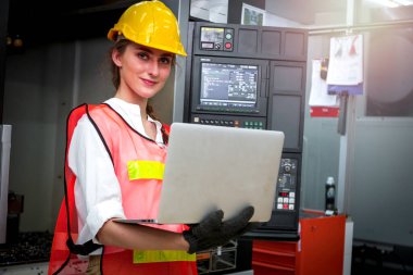 Sanayi mühendisi kadın, kask takıyor ve imalat fabrikasında dizüstü bilgisayar kullanıyor. Endüstride çalışan genç ve güzel bir kadın.