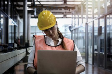 Fabrika imalatında dizüstü bilgisayar kullanan endüstriyel mühendis kadın kask takıyor. Endüstride çalışan genç ve güzel bir kadın.