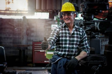 Kask ve güvenlik gözlüğü takan endüstri mühendisi, koruyucu eldiven takan ve başparmak kaldıran işçi, fabrika imalatında makine ile çalışan, endüstri konseptinde çalışan makineler.