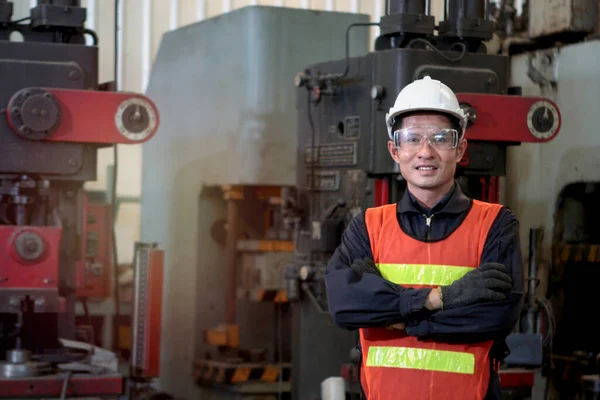 Industrial engineer worker wearing helmet and safe glasses standing with arms crossed at manufacturing plant factory, working with machine in industry concept