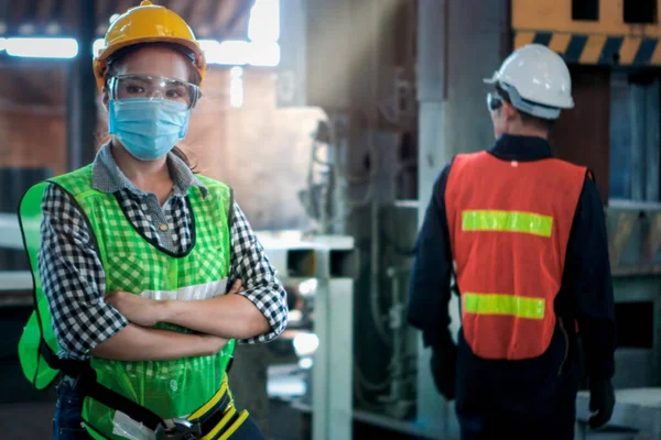 Industrial engineer worker wearing helmet, safe glasses and mask with arms crossed at manufacturing plant factory, young beautiful woman working in industry