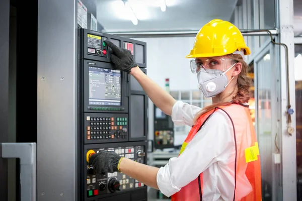 Industrial engineer worker female wearing helmet, safe glasses and mask, pointing and touching instrument panel buttons at manufacturing plant factory, young beautiful woman working in industry