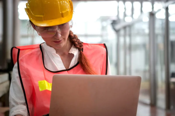 在制造厂 女工业工程师戴着头盔 使用笔记本电脑 年轻漂亮的女士在工厂工作 — 图库照片