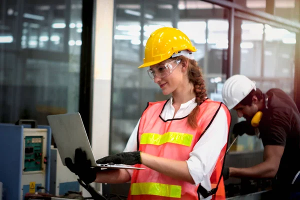 Industrial engineer worker wearing helmet and safe glasses, holding laptop compute, working with instrument at manufacturing plant factory, young beautiful woman working in industry