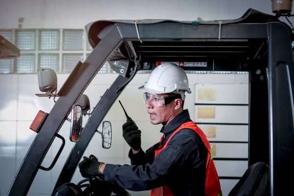 Industrial engineer worker wearing helmetand safe glasses, holding radio walkie talkie, driving forklift car at manufacturing plant factory industry concept
