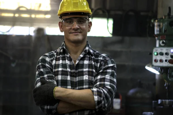 Portrait of industrial engineer worker wearing helmet and safe glasses standing with arms crossed at manufacturing plant factory