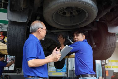 Two mechanic checking wheel and inspecting car under body and suspension system at garage, technician check and repair customer car at automobile service, senior and young work together. 