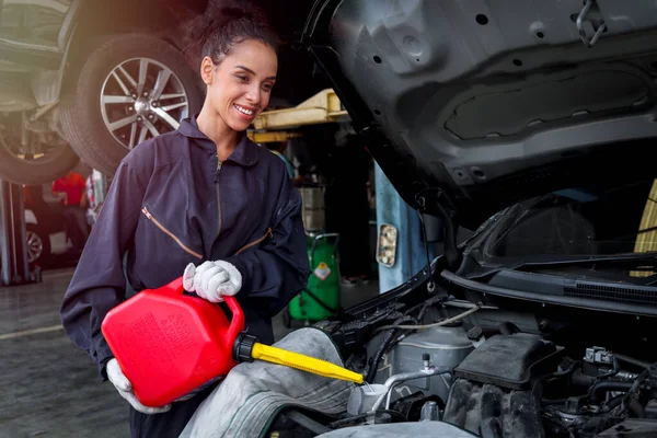 Female mechanic with motor oil gallon working in garage, car service technician checking and repairing customer car at automobile service center, vehicle repair service shop concept