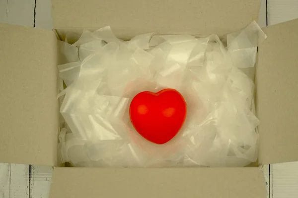 Red heart in parcel box with shredded paper, packing and sending Love on Valentine\'s day concept