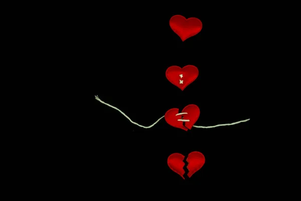 Healing broken heart concept, red heart is sewn with  white thread with needle on black background.