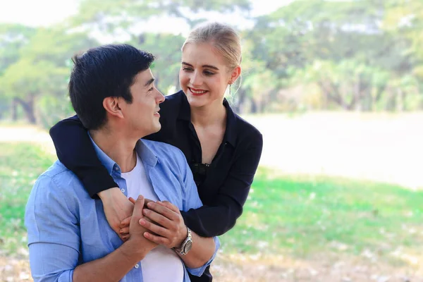 Sweet couple showing love each other in park, young beautiful woman puts her arms around her boyfriend\'s neck, lover hugging each other while spending time together and having romantic moment in summer garden