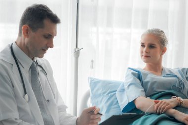 Doktor, genç ve güzel hastayı muayene ediyor ve hastane yatağında yatan hastaya sağlık sorunlarını anlatıyor.