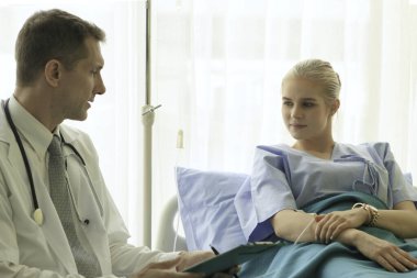 Doktor, genç ve güzel hastayı muayene ediyor ve hastane yatağında yatan hastaya sağlık sorunlarını anlatıyor.