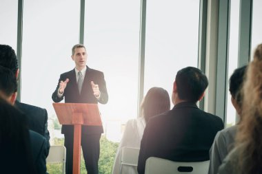 Başarılı iş adamı tecrübelerini paylaşıyor ve konuşma yapıyor. Bir grup iş adamı konferansta birlikte oturup toplantı odasındaki konuşmacıyı dinliyor..