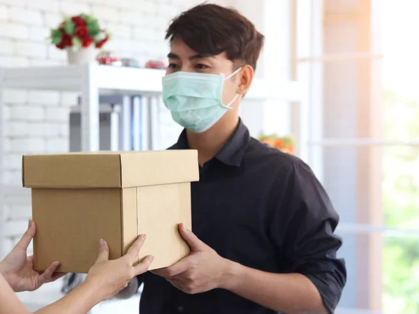 Hands deliver the goods to the recipient customer. Young man wearing face mask receiving delivery parcel box to prevent covid19 infection, social distancing and new normal shipping and courier delivery services express concept.