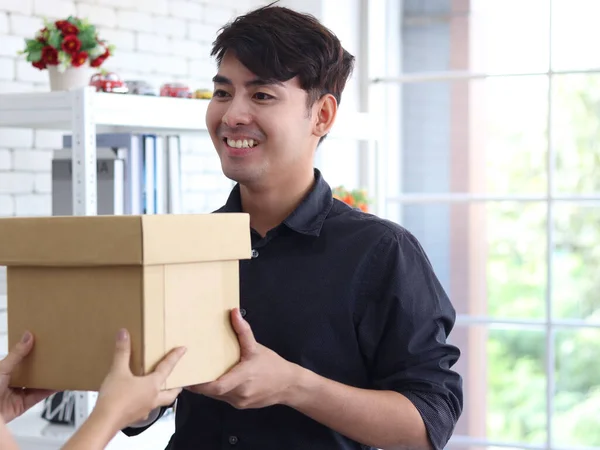 Hands deliver the goods to the recipient customer. Young man receiving delivery parcel box, shipping and courier delivery services express concept.