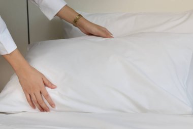 Oda servisi temizliği ve otel odası konsepti, otel odasında yatak yapmak için yastık tutan oda hizmetçisinin kadın elleri..
