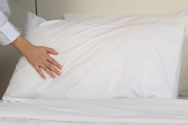 Oda servisi temizliği ve otel odası konsepti, otel odasında yatak yapmak için yastık tutan oda hizmetçisinin kadın elleri..