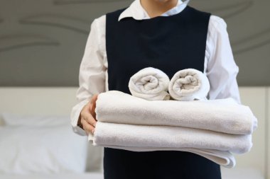Oda servisi temizliği ve otel odası konsepti. Kadın oda hizmetçisi otel odasında yatak yapmak için temiz beyaz banyo havluları tutuyor..